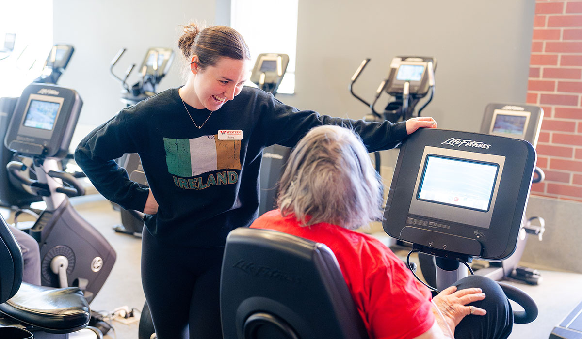 Student facilitates a workout for an elderly community member on an exercise bike