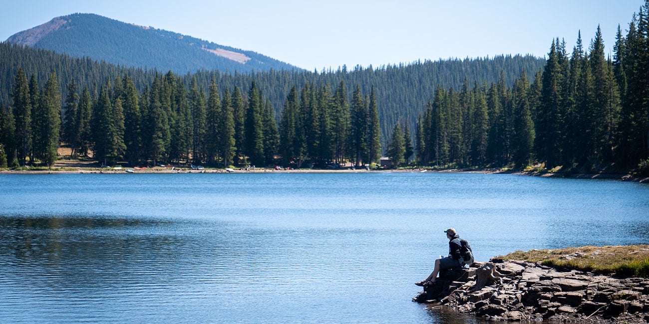 A student sits near the edge of a mountain lake