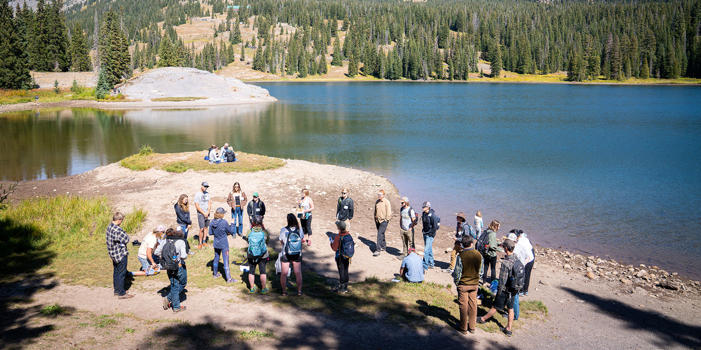 Several students gather near an alpine lake during a headwaters session