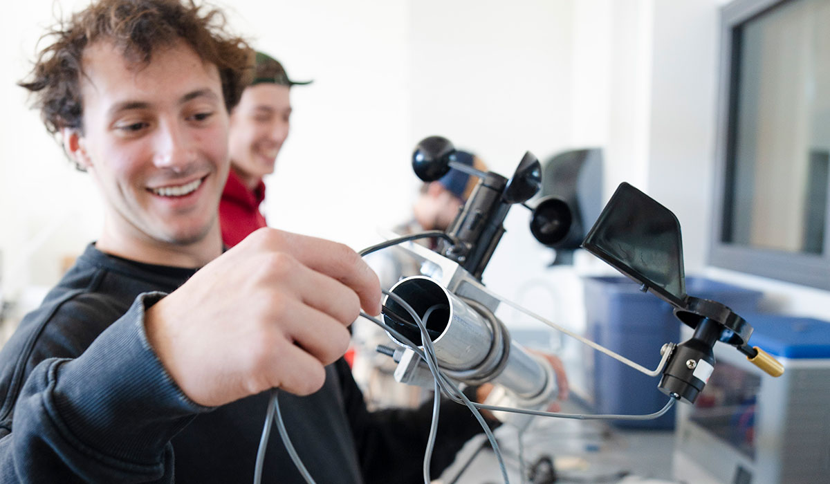 Engineering student feeds wire down a metal pipe of sensor suite he's helping build for Rocky Mountain Biological Laboratory