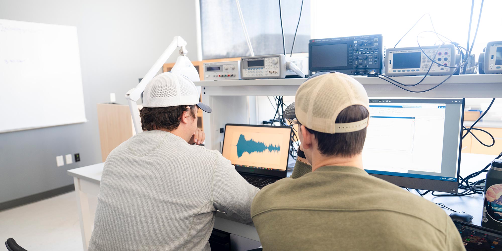 Two engineering students work together looking at programs and graphs on computer screens