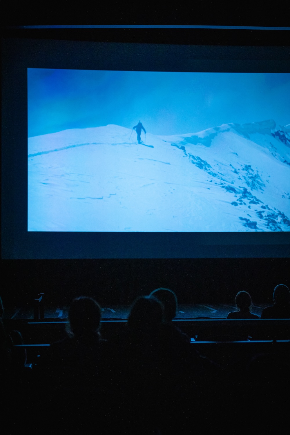 Students in the UC Theater watch the Spirit of the Peaks film. An image of Connor Ryan skinning on a windy ridgeline appears on the screen.