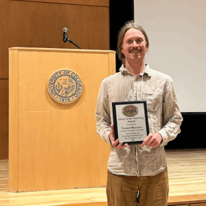 Dr. Forest Mannan poses with his award in front of a stage.