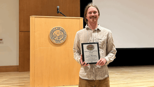 Dr. Forest Mannan poses with his award in front of a stage.