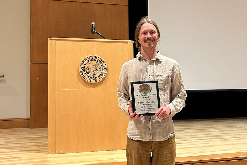Dr. Forest Mannan poses with his award in front of a stage.
