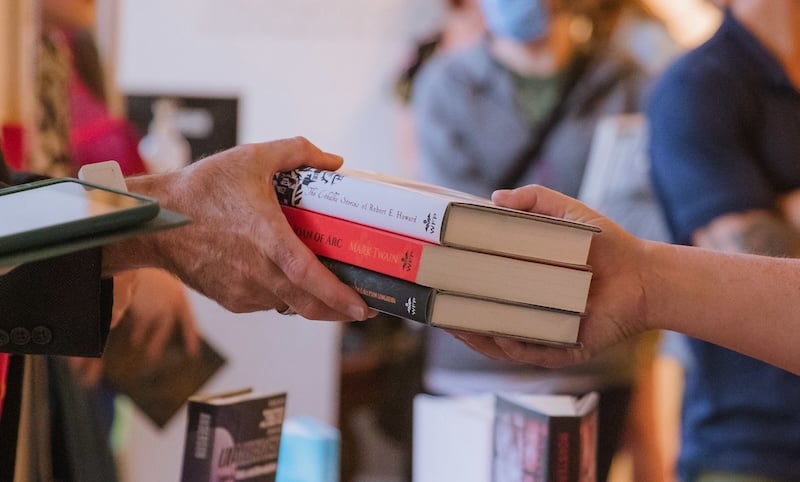 A person hands over a pile of books while making a transaction during the publishing student's book signing.