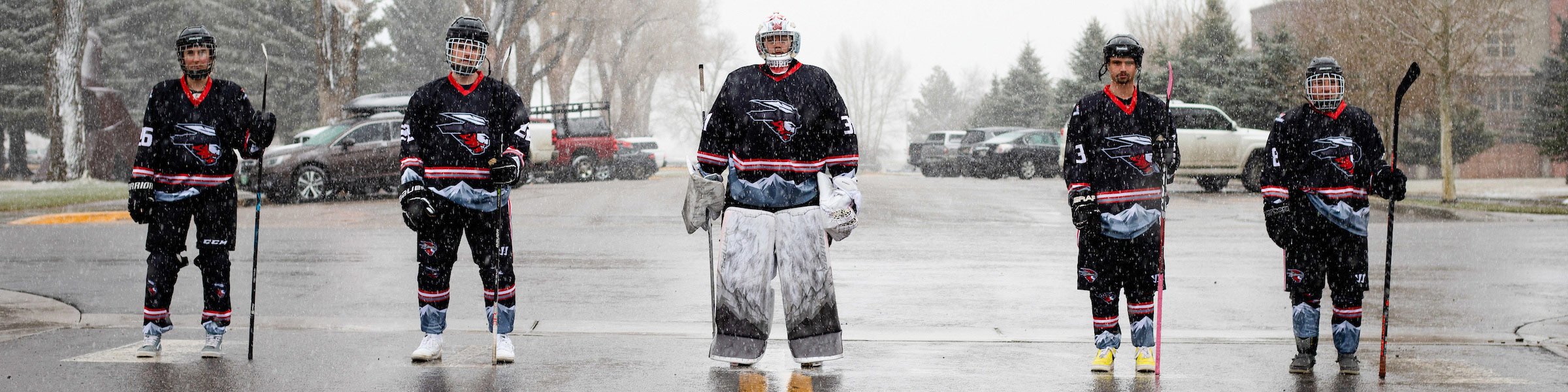 A photo of five Western hockey players standing evenly spaced out on a crosswalk across a road while it snows.