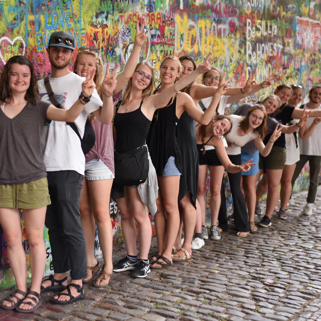 Honors students pose with peace signs against a mural.