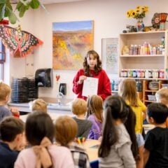 A student teacher holds up a coloring sheet in front of the first grade art class.