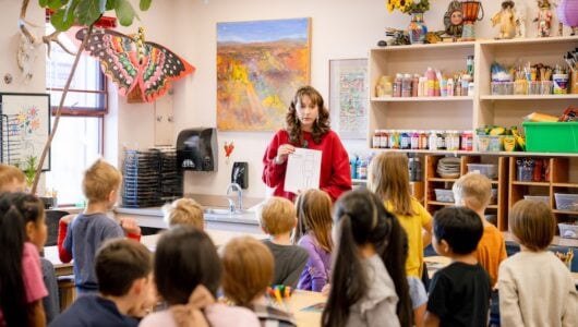 A student teacher holds up a coloring sheet in front of the first grade art class.