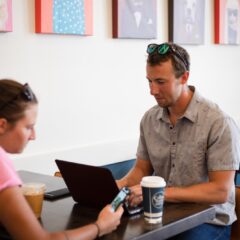 Mike Braun types on a laptop while sitting at a table with Eliza Lockhart at The Coffee Trader.