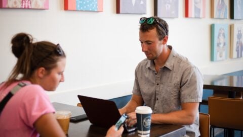 Mike Braun types on a laptop while sitting at a table with Eliza Lockhart at The Coffee Trader.