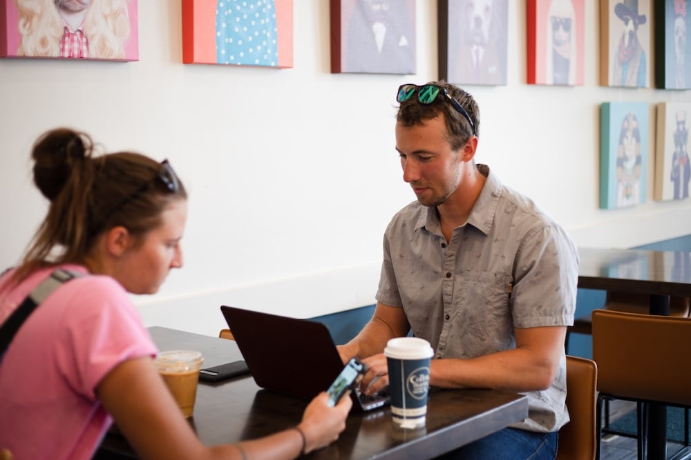 Mike Braun types on a laptop while sitting at a table with Eliza Lockhart at The Coffee Trader.