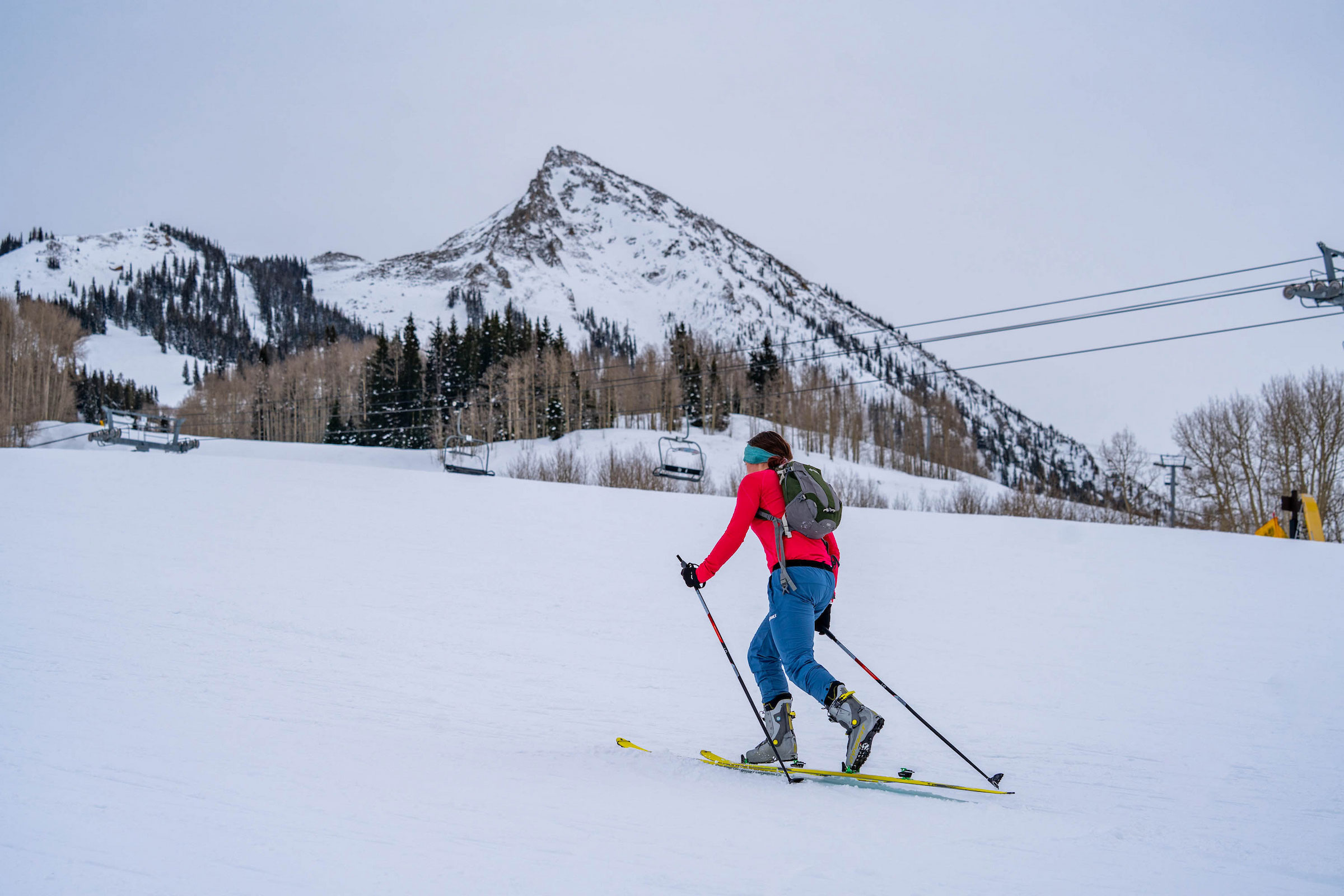 A female Western skimo athlete skins up the uphill route at Crested Butte Mountain Resort with the peak of Mt. Crested Butte in the background.