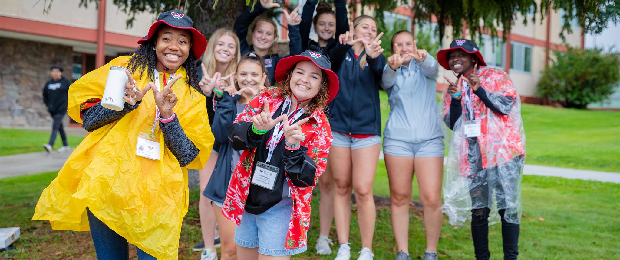Orientation leaders and members of the women's soccer team gather for a group photo with their hands giving the W symbol in front of the Escalante Complex