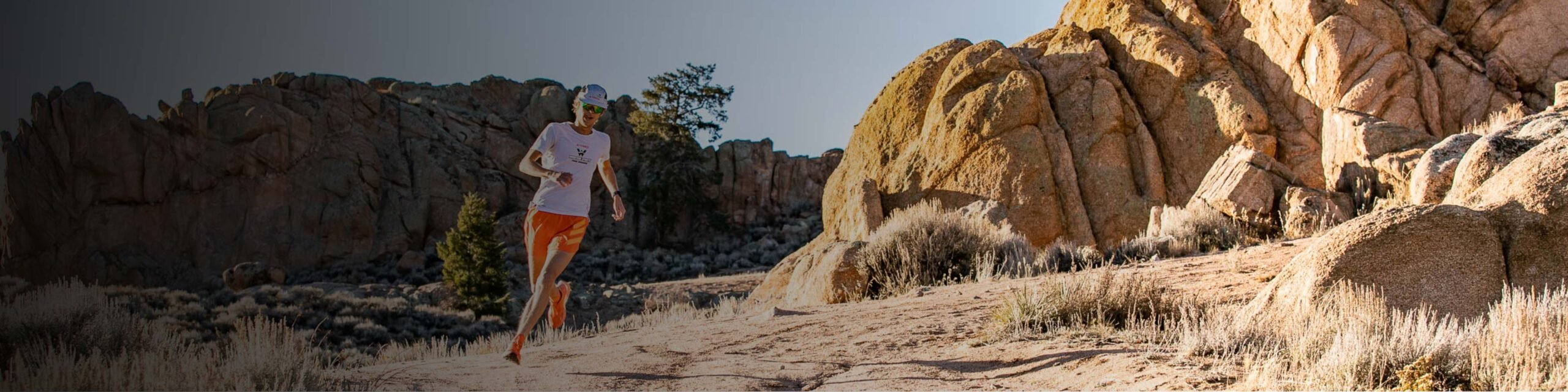 A student wearing an adidas uniform trail runs at Hartman Rocks at golden hour.