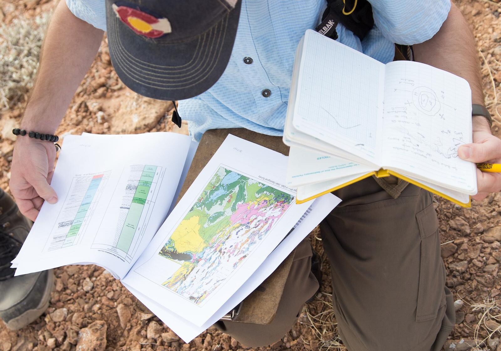 A geology student on a field trip reads a map while holding their field notebook.