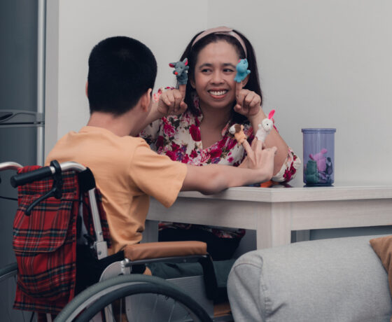 A female student teacher demonstrates a lesson for a student in a wheelchair.