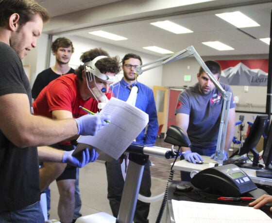 Four students observe a person hooked up to lab equipment using a stationary bike.