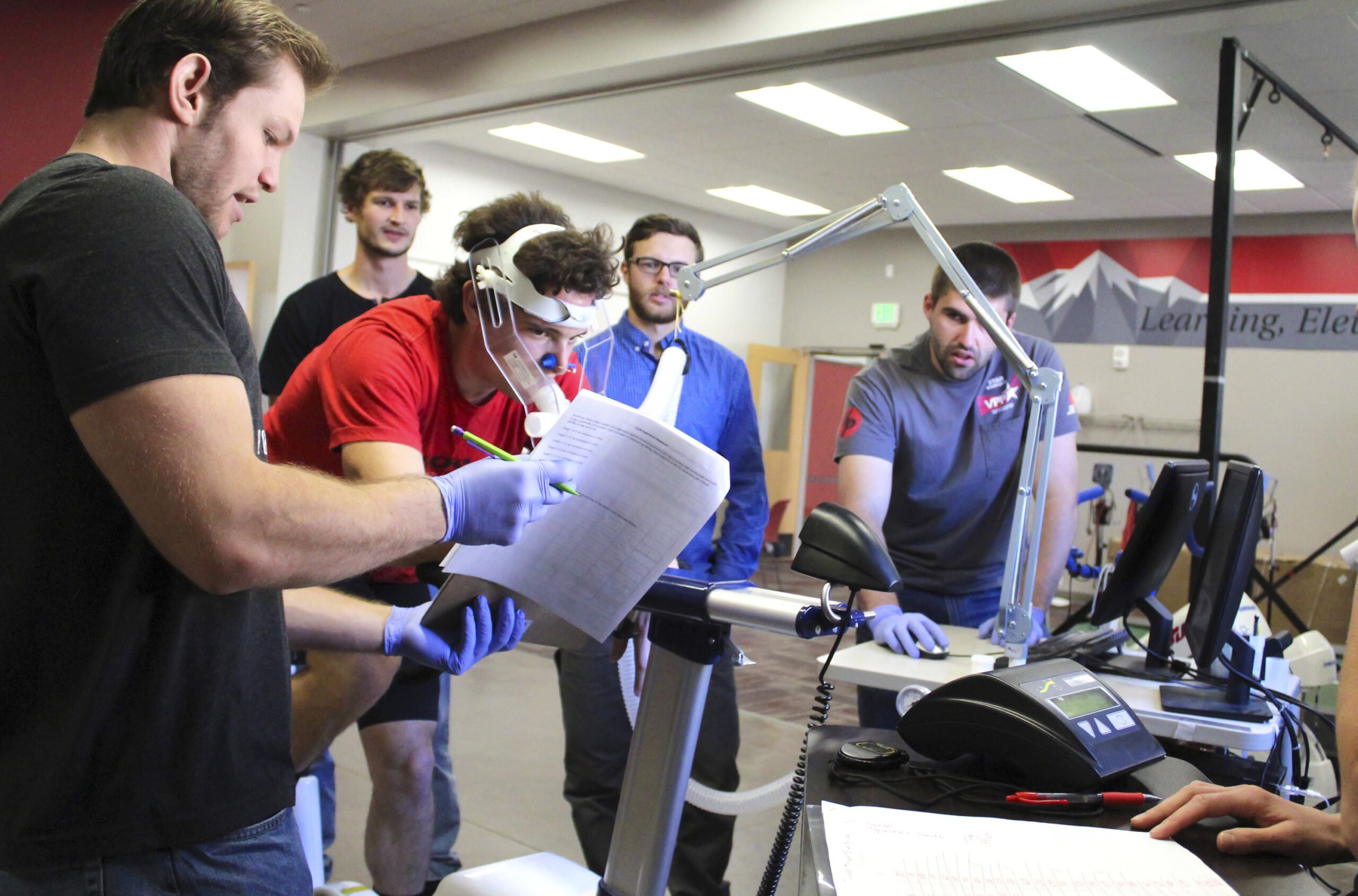 Four students observe a person hooked up to lab equipment using a stationary bike.