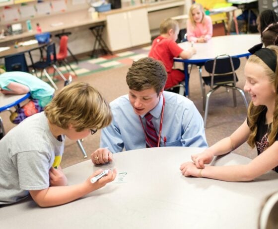 A student teacher collaborates with elementary students in a classroom.