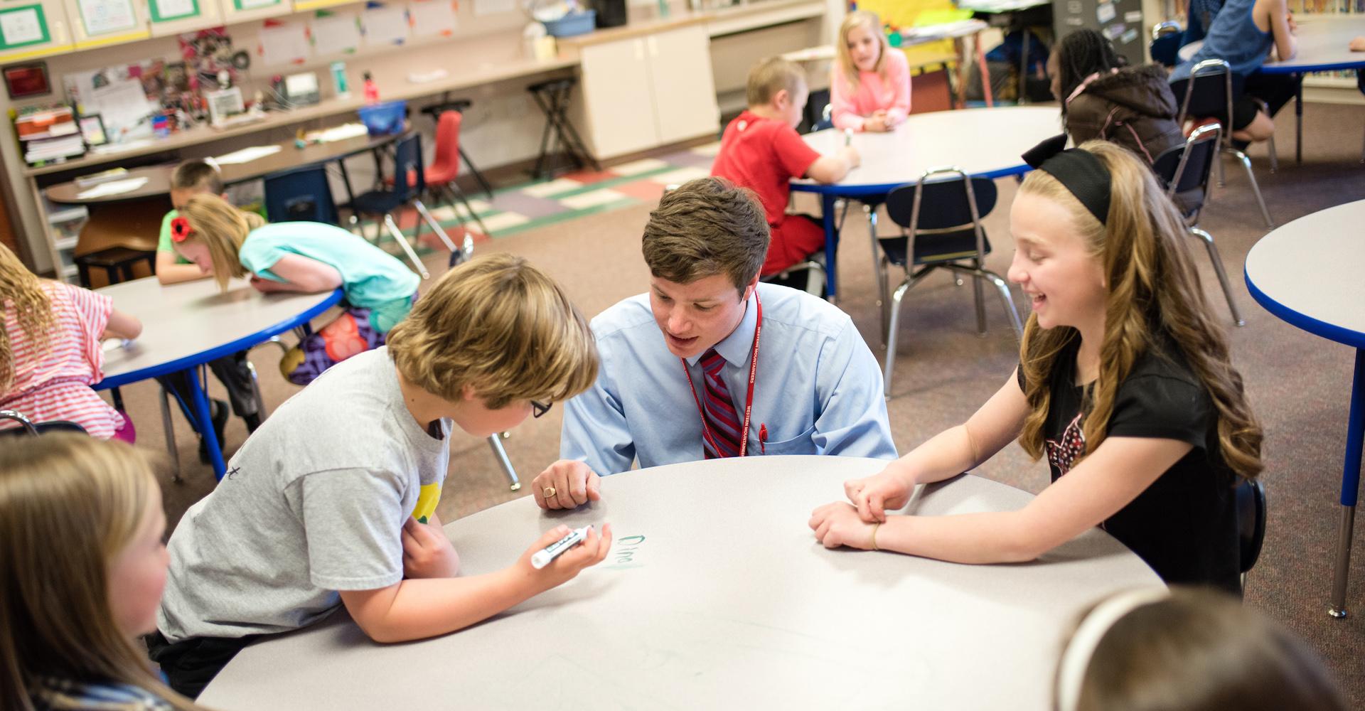 A student teacher collaborates with elementary students in a classroom.