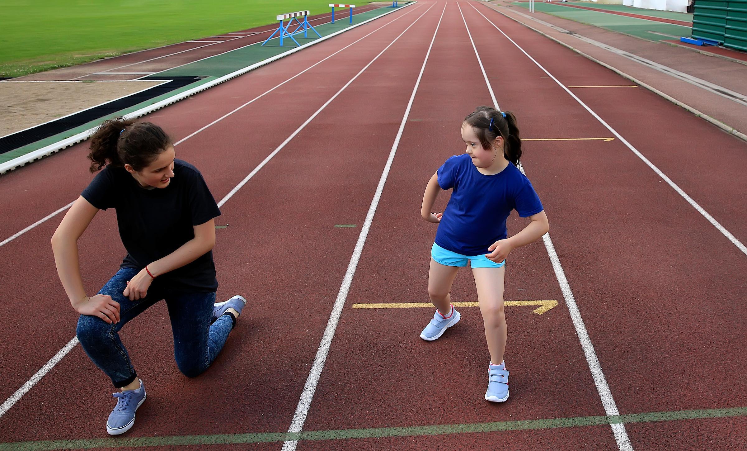 A teacher and student practice stretching on an outdoor track.