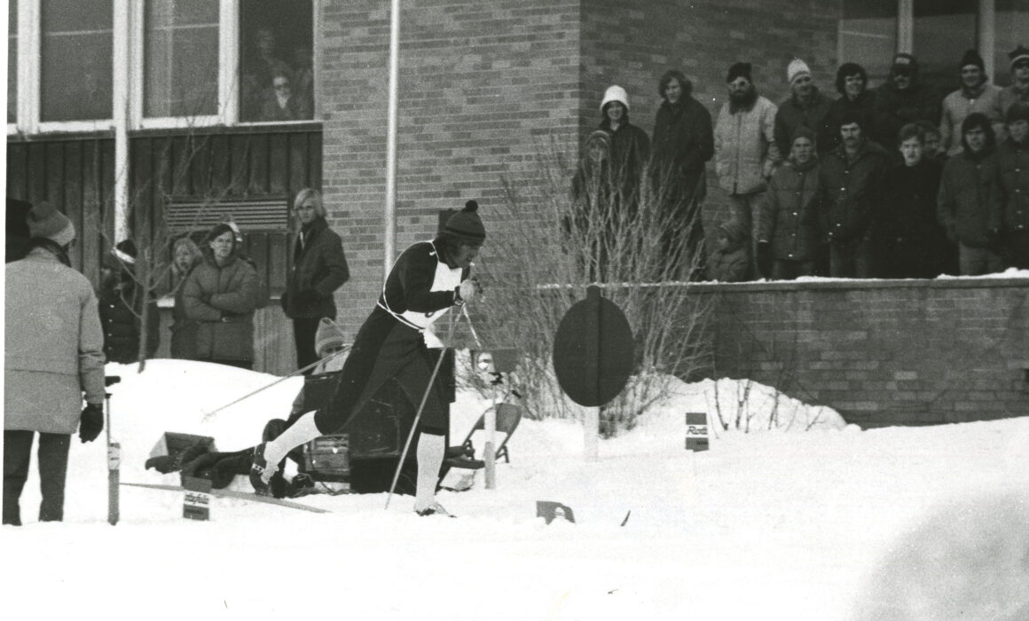 A cross country ski competitor skis by spectators in front of the WSC Student Union, 1980s.