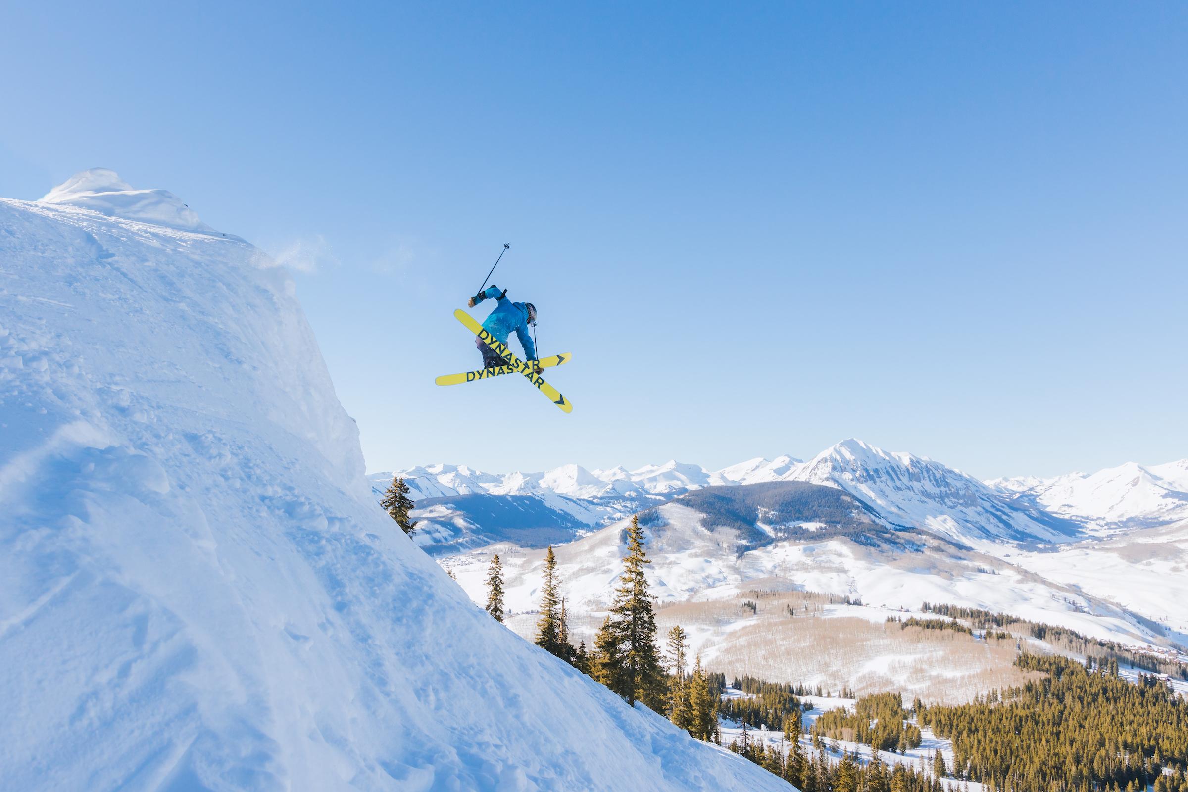 A skier grabs his skis while dropping off a cliff at Crested Butte Mountain Resort